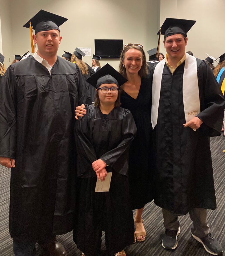 A group of people including two college graduates stand facing the camera.