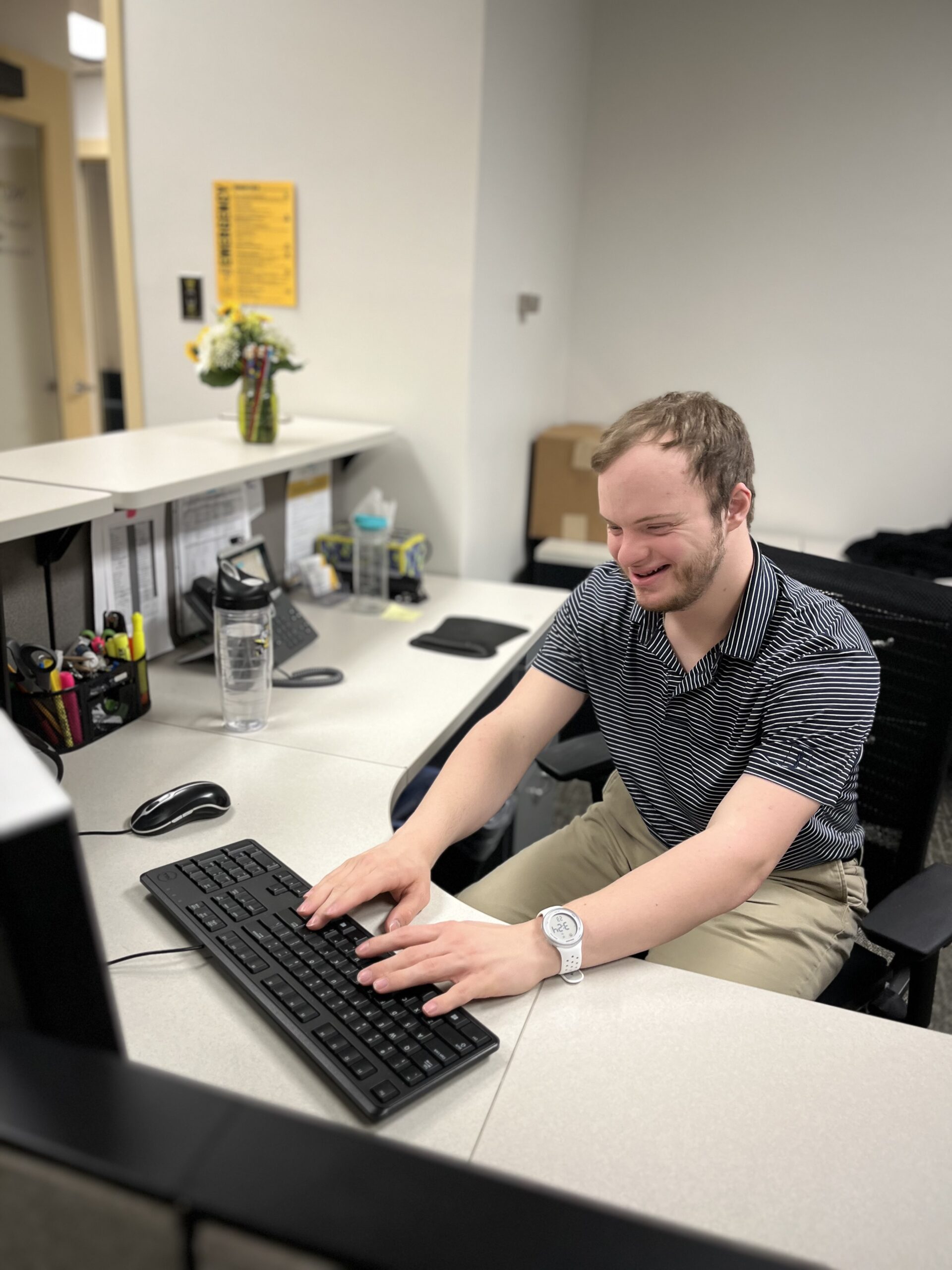 A smiling Nate sits at a workstation, typing on a computer keyboard.