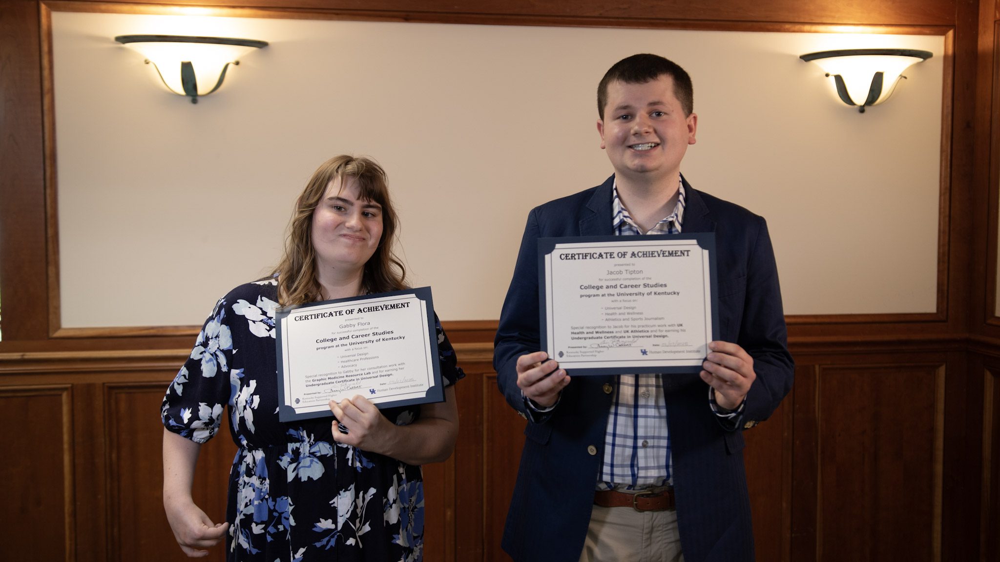 Gabby and Jacob stand in a formal room with their certificates of completion.